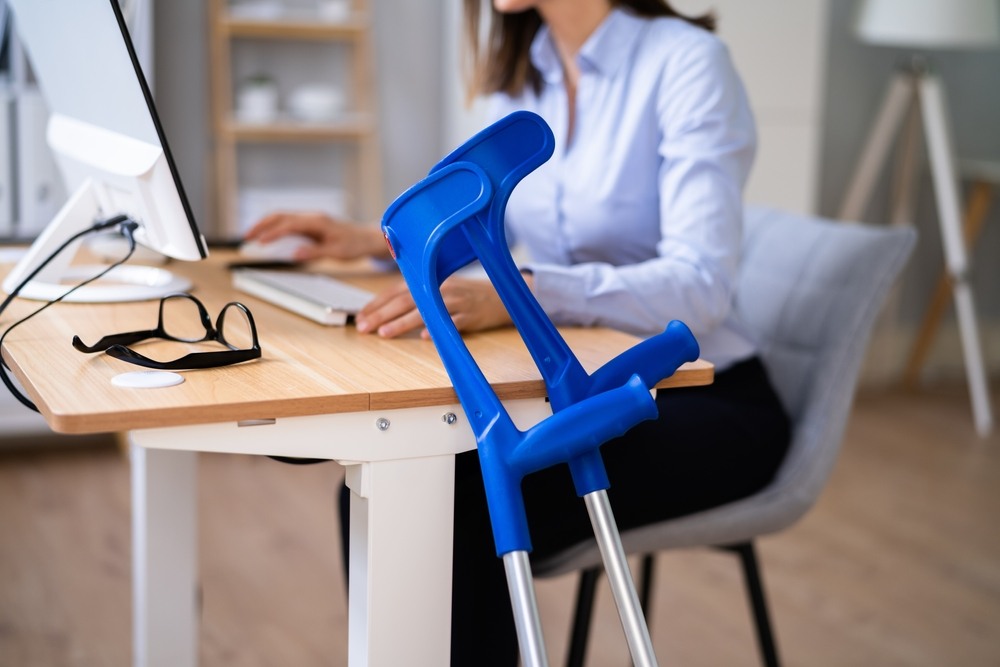 Crutches leaning against an office desk while an injured worker returns to modified duty at her computer