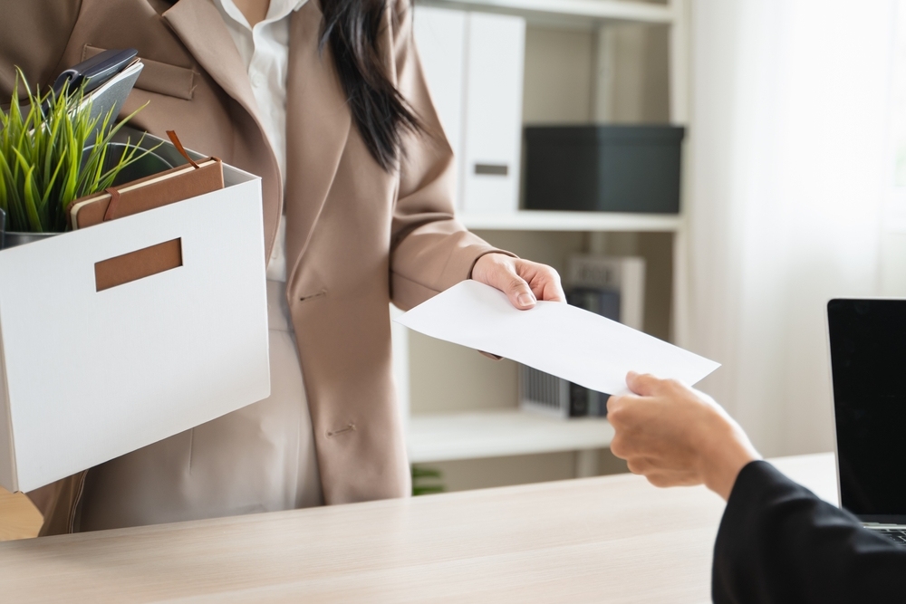 Employee holding a box of personal belongings while receiving a termination letter after filing a workers compensation claim