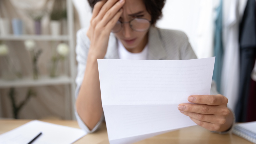 Woman reading a letter with a distressed expression, holding her head after receiving a termination notice