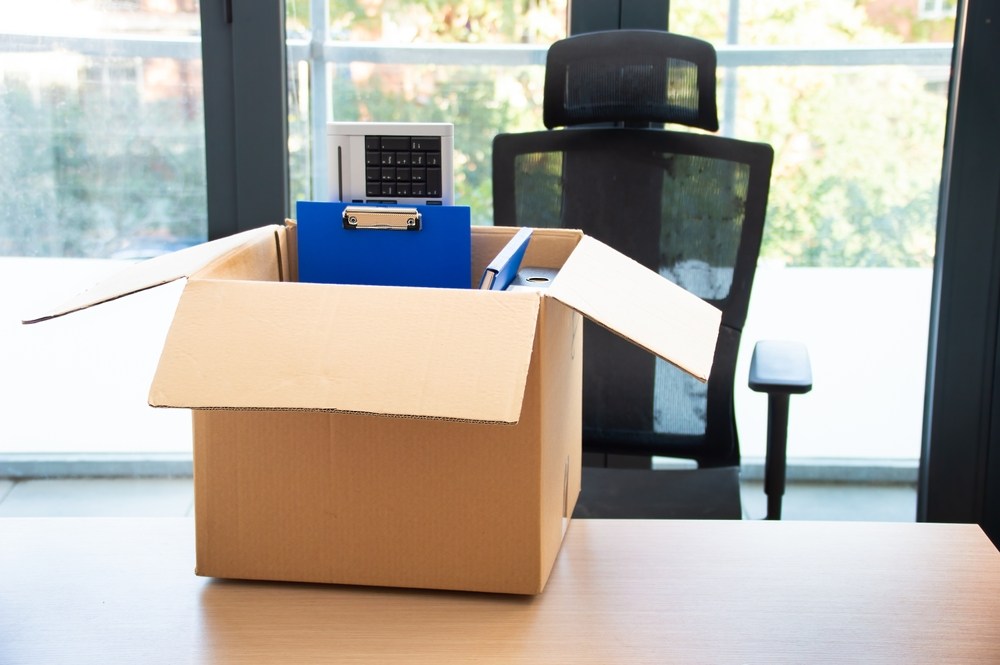 Cardboard box filled with office supplies and files sitting on an empty desk after a termination
