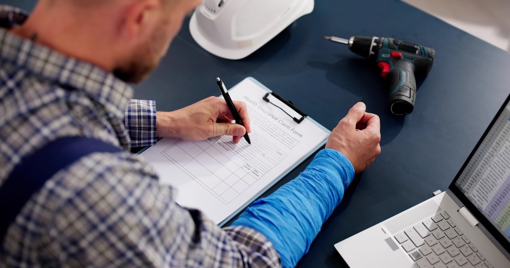 Worker filling out a workers' compensation claim form beside a hard hat and power drill